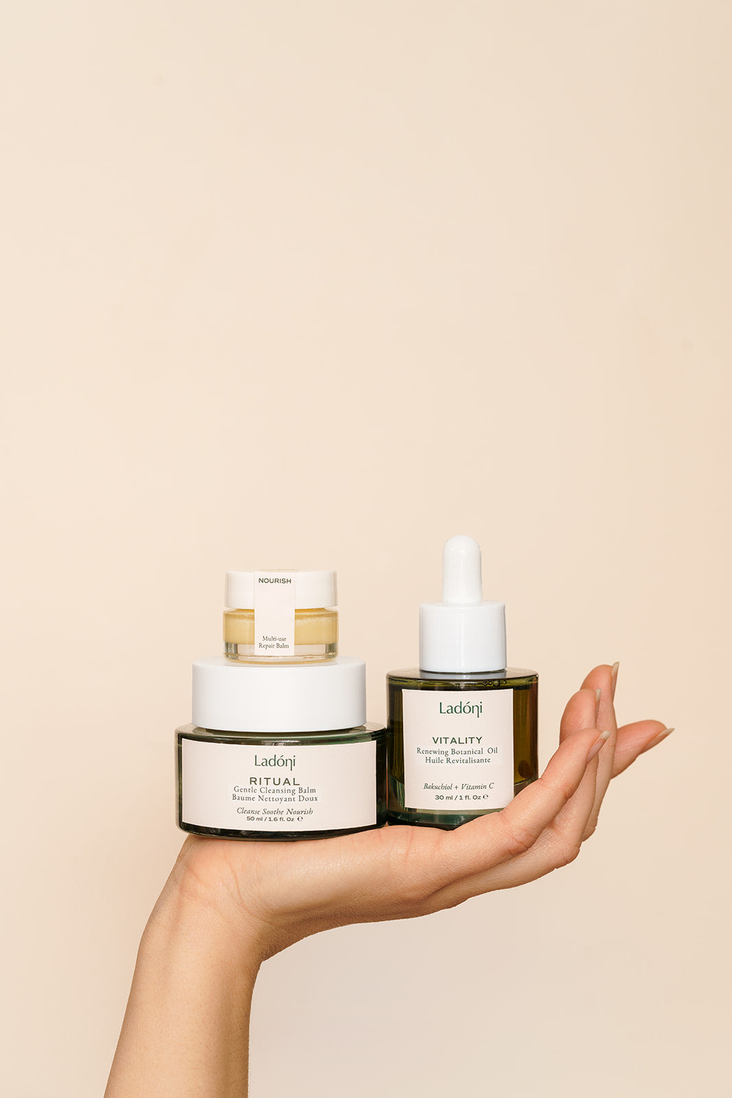 Ladoni's face oil, balm cleanser and lip balm held by a hand with a beige background 